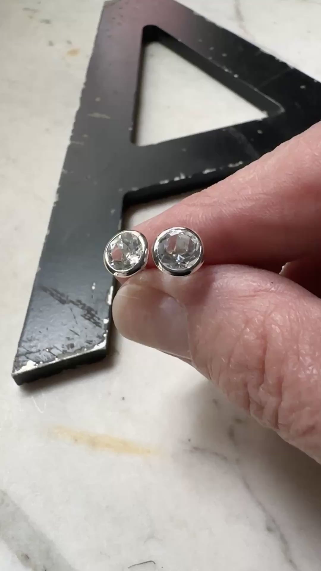 a pair of 6mm white topaz bezel set stud earrings resting on a marble surface