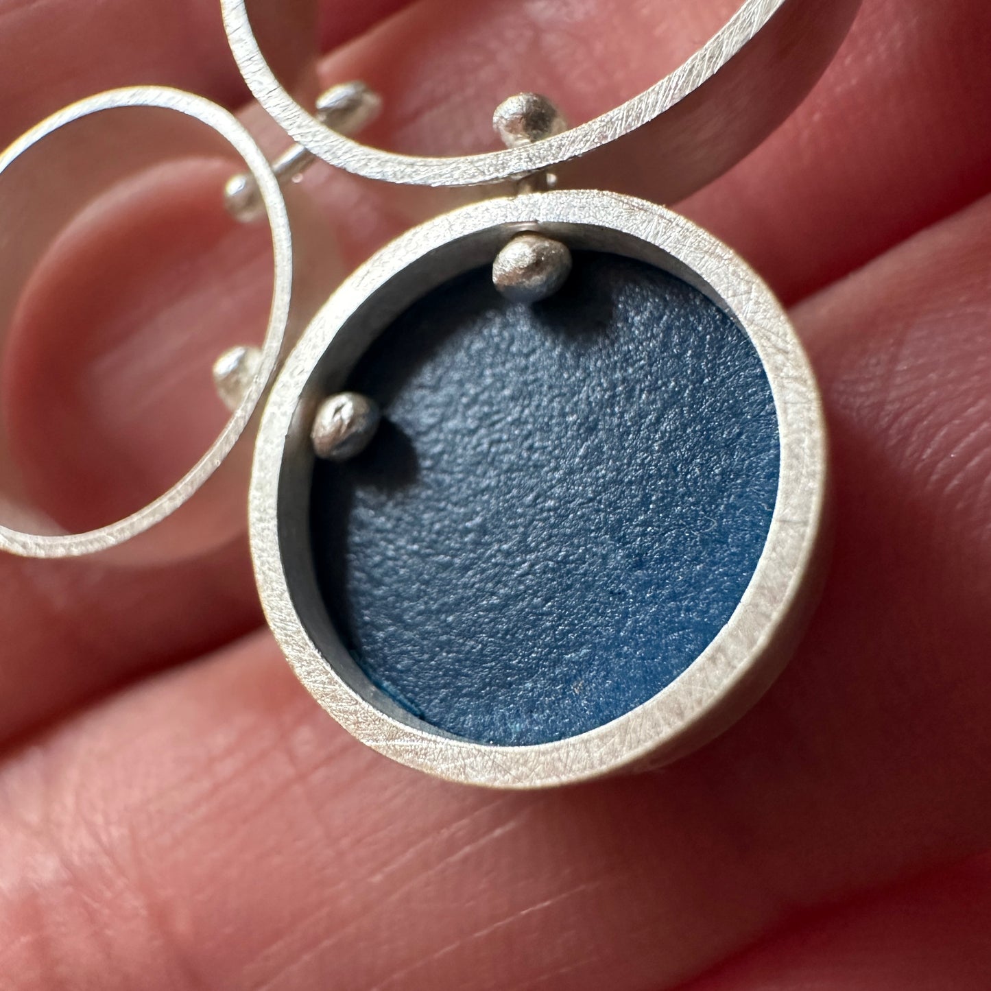 A close up of a pair of silver post  earrings with cellular drop elements featuring small round blue formica, displayed on a light marble surface.
