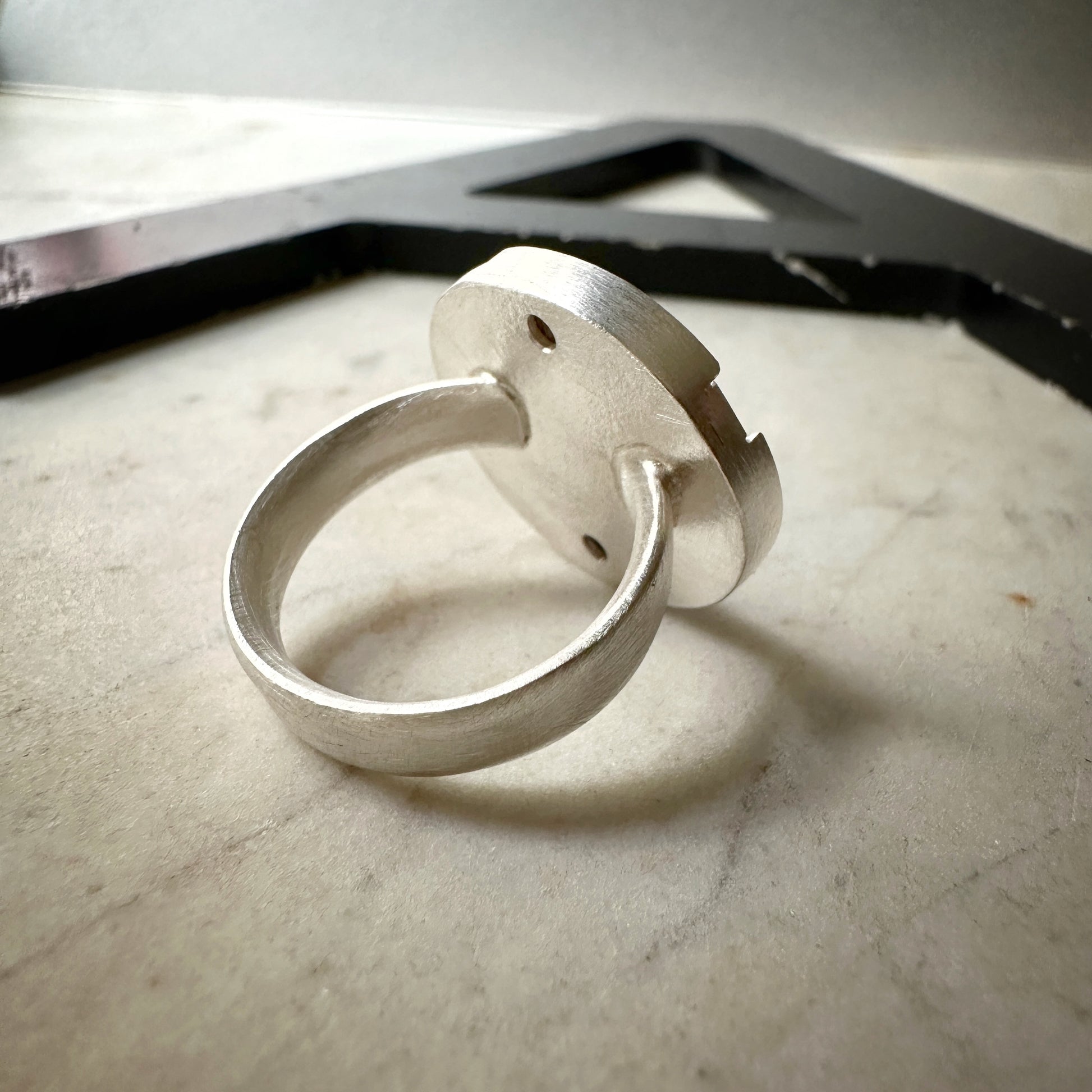 A sterling silver ring with a circular, disc-like back and a thick band, resting on a light marble surface.