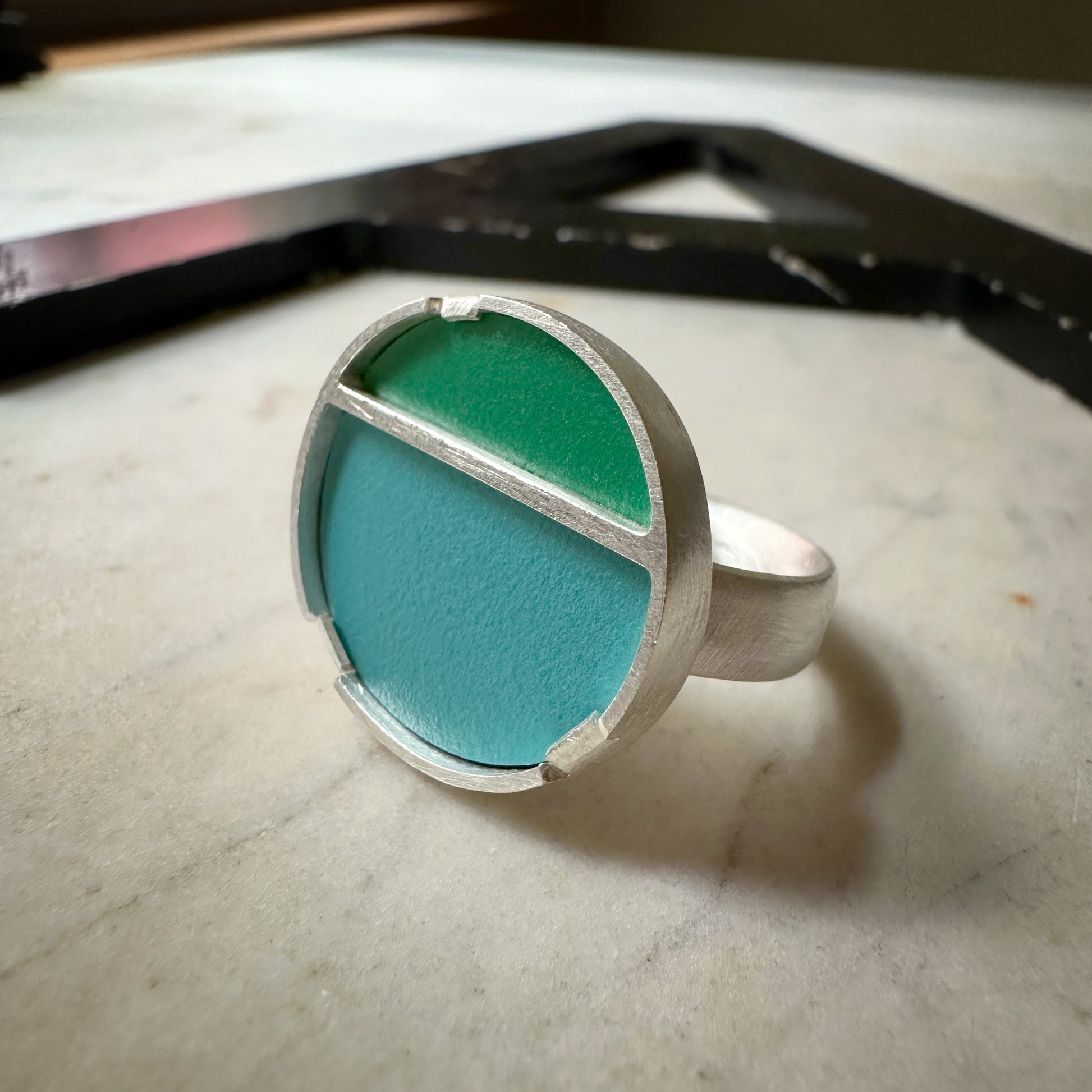A sterling silver ring with a circular face with green formica on top and blue formica on the bottom 