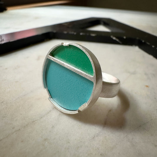 A sterling silver ring with a circular face with green formica on top and blue formica on the bottom 