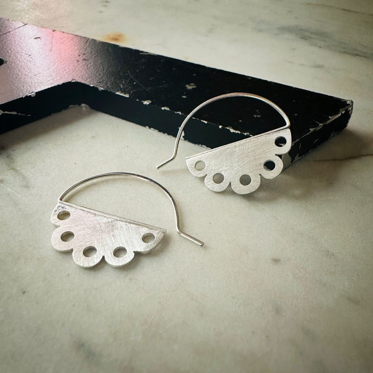 one pair of scalloped hoop earrings with a pierced design in bright silver 