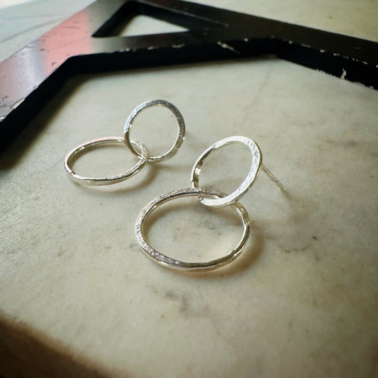 A pair of textured silver hoop earrings resting on a light beige marble surface.