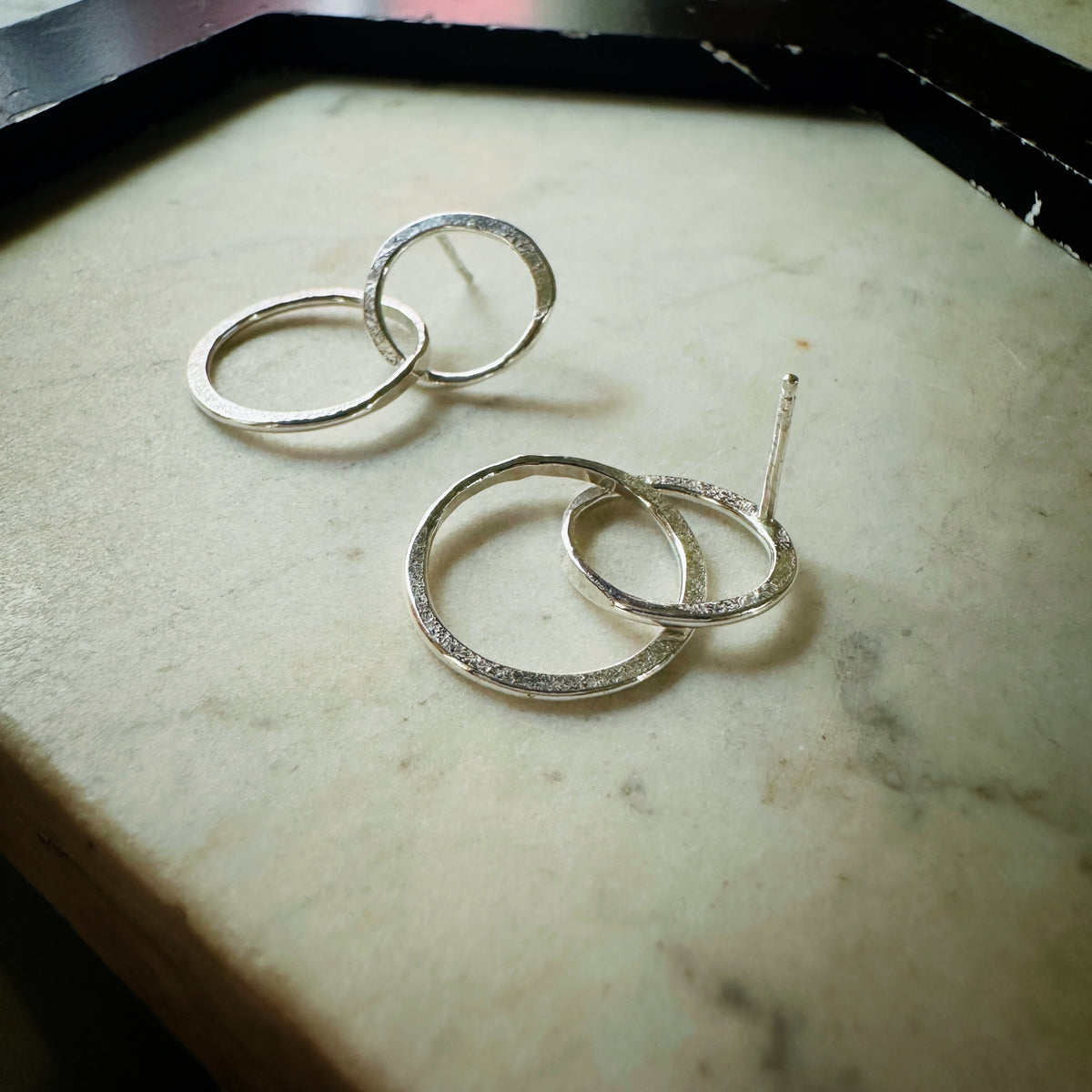 A pair of textured silver hoop earrings with post backs, displayed on a light beige stone surface.