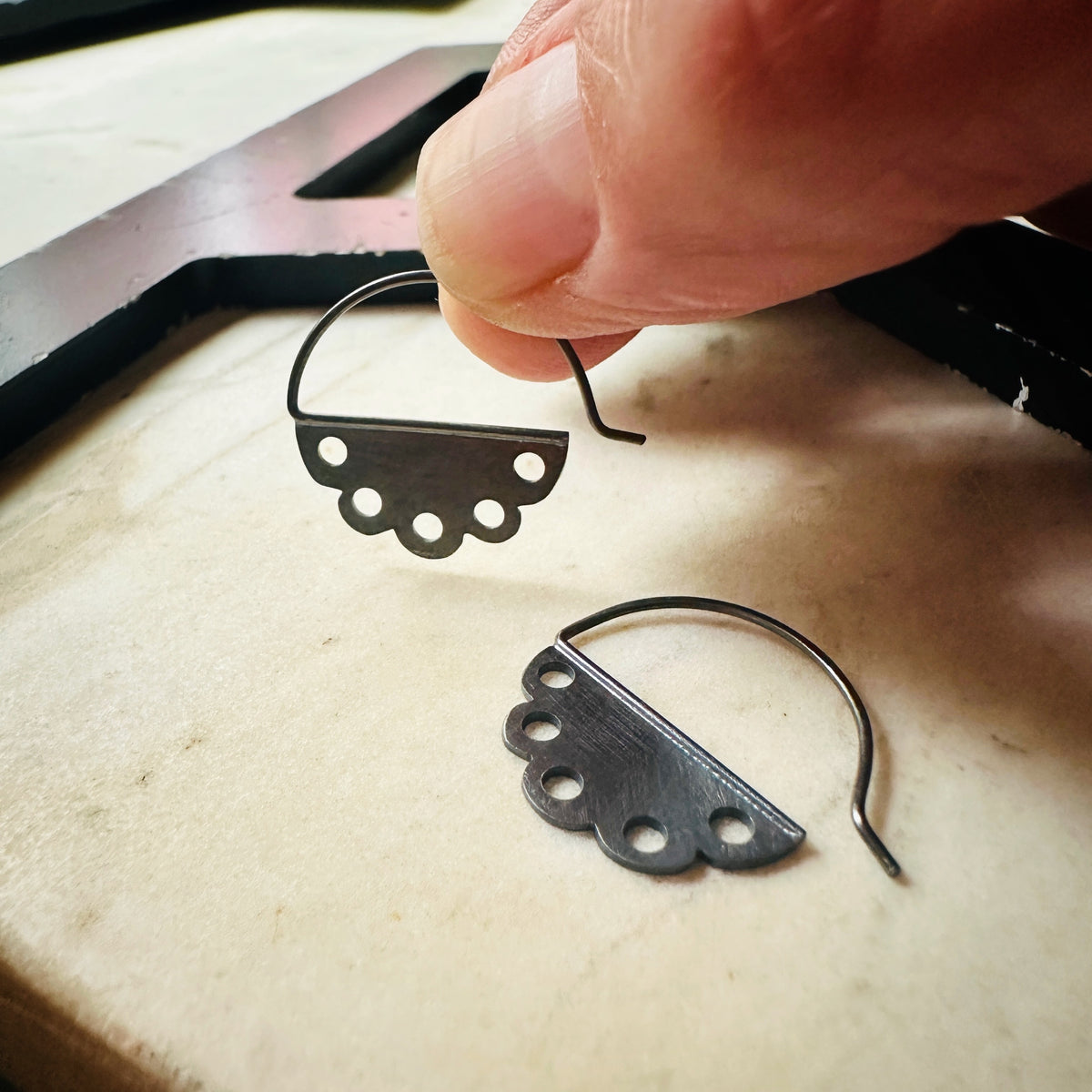 one pair of oxidized silver scalloped edge hoop earrings being held in a hand for scale 