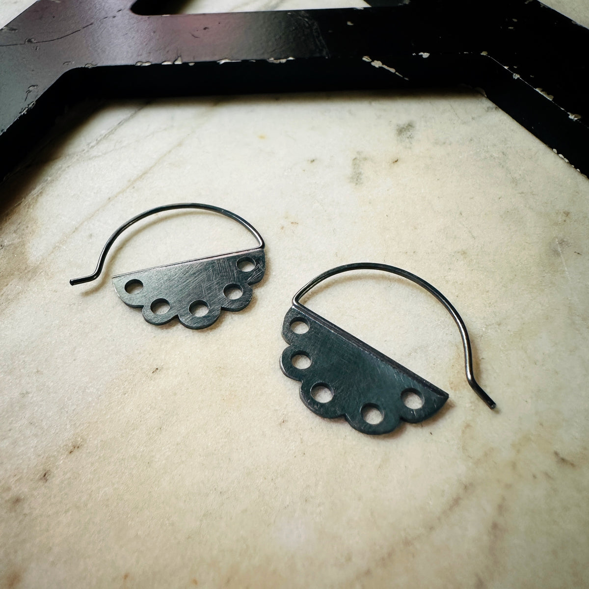 one pair of scalloped earrings with pierced design in oxidized silver