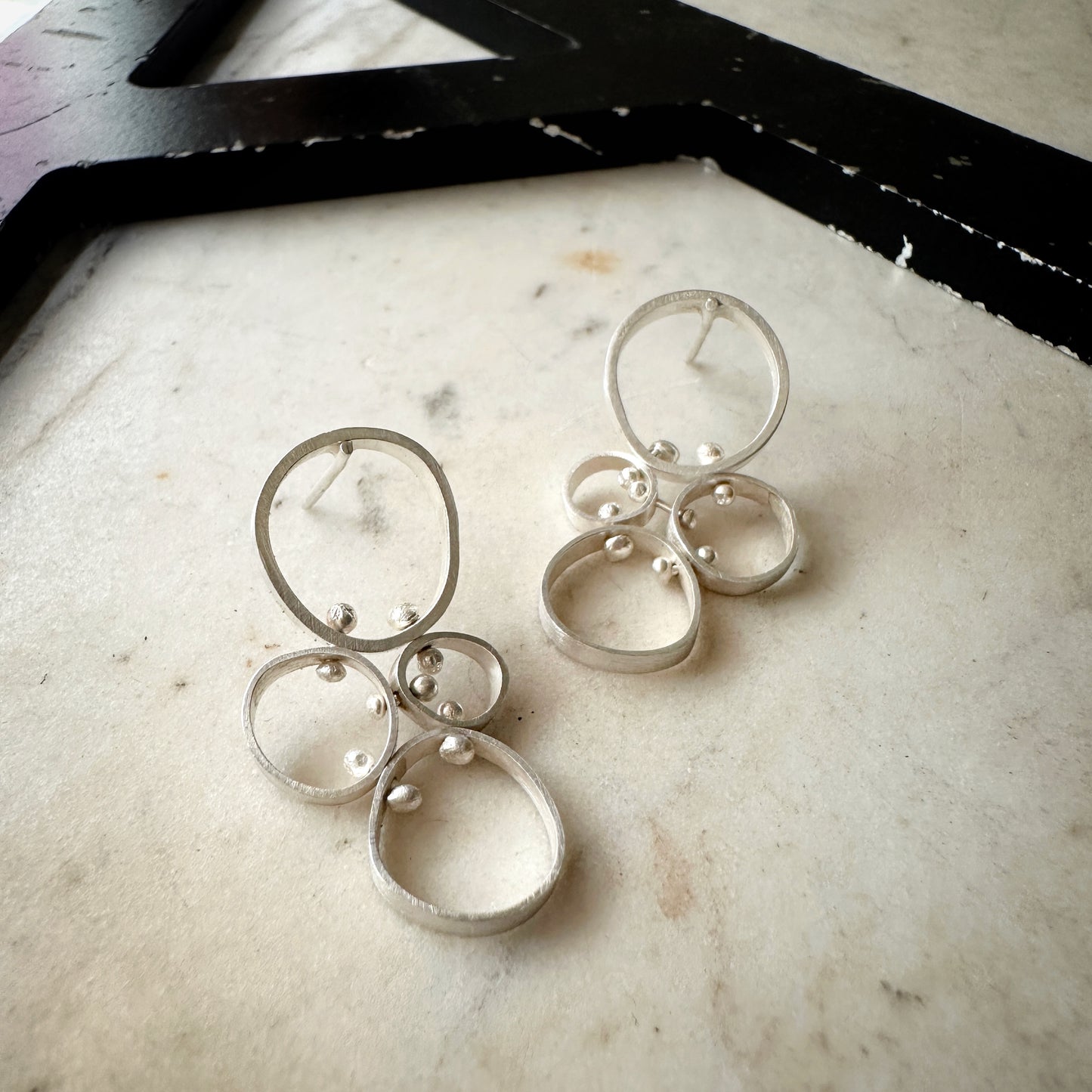 A pair of silver-toned geometric dangle earrings with overlapping circular rings and small bead details, displayed on a light marble surface.
