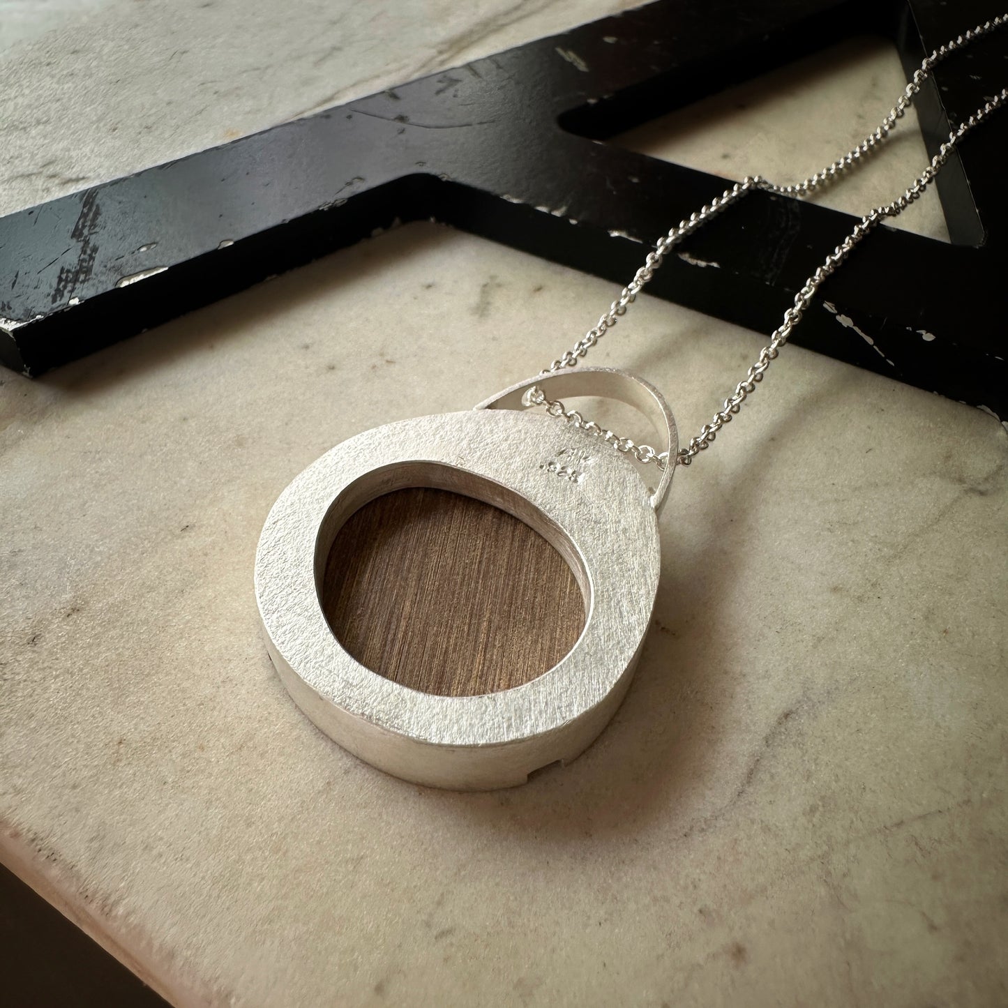 The sterling silver oval pendant back showing a cut out and the wood formica backing 