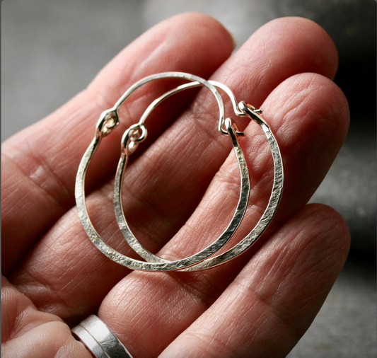 a hand holding a pair of 1 inch sterling hoop earrings with a top latch and hammered texture