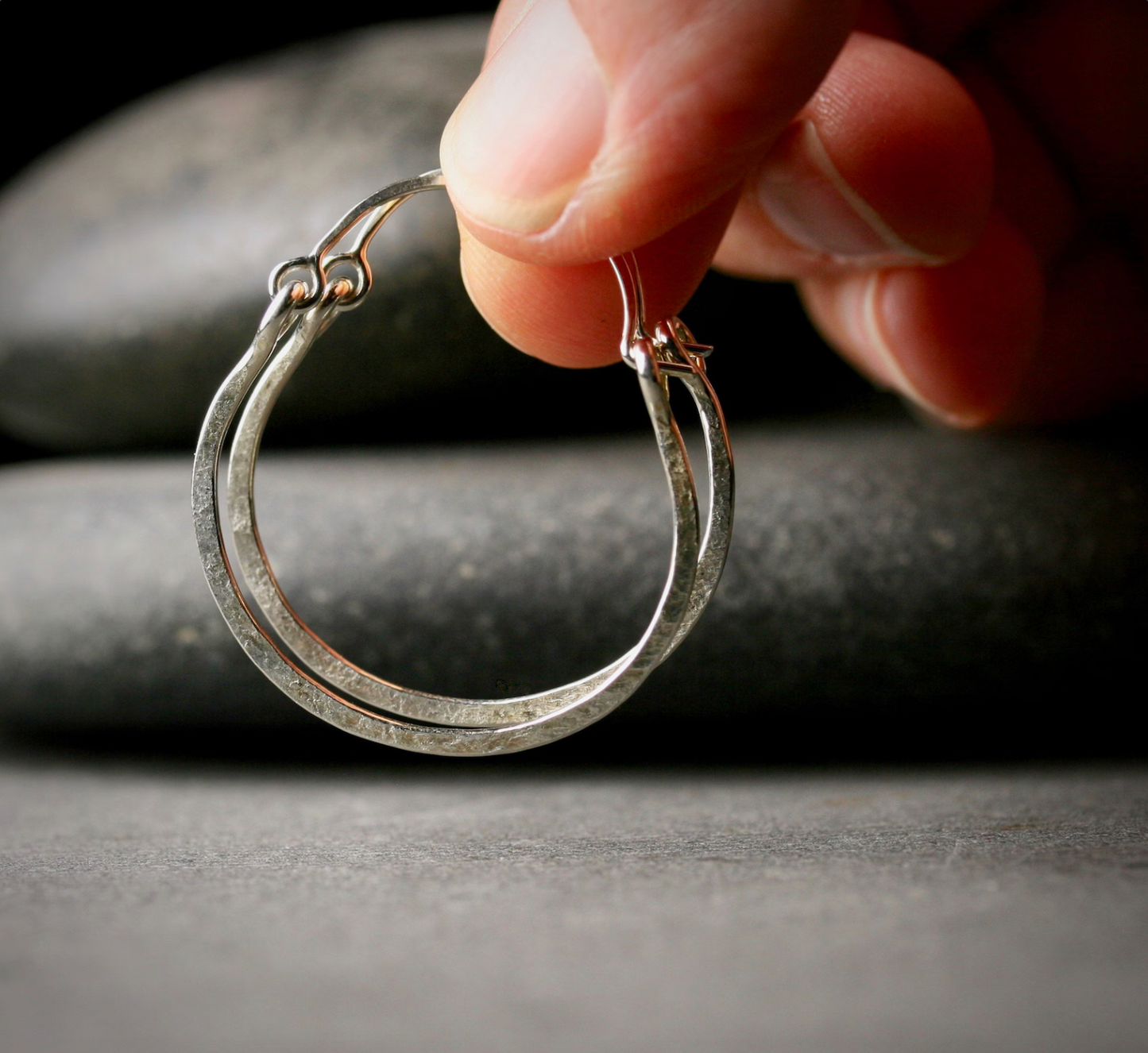 a hand holding a pair of 1 inch sterling silver hoops, shaped like kettles with a top catch