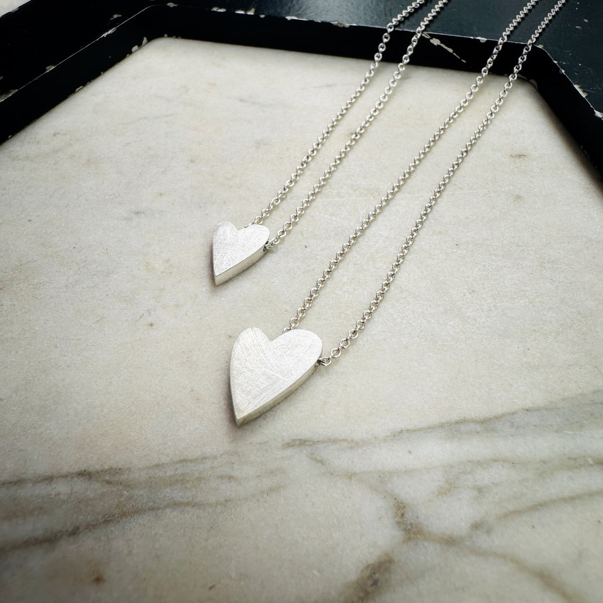two sterling silver heart pendants in sterling silver on a marble surface 