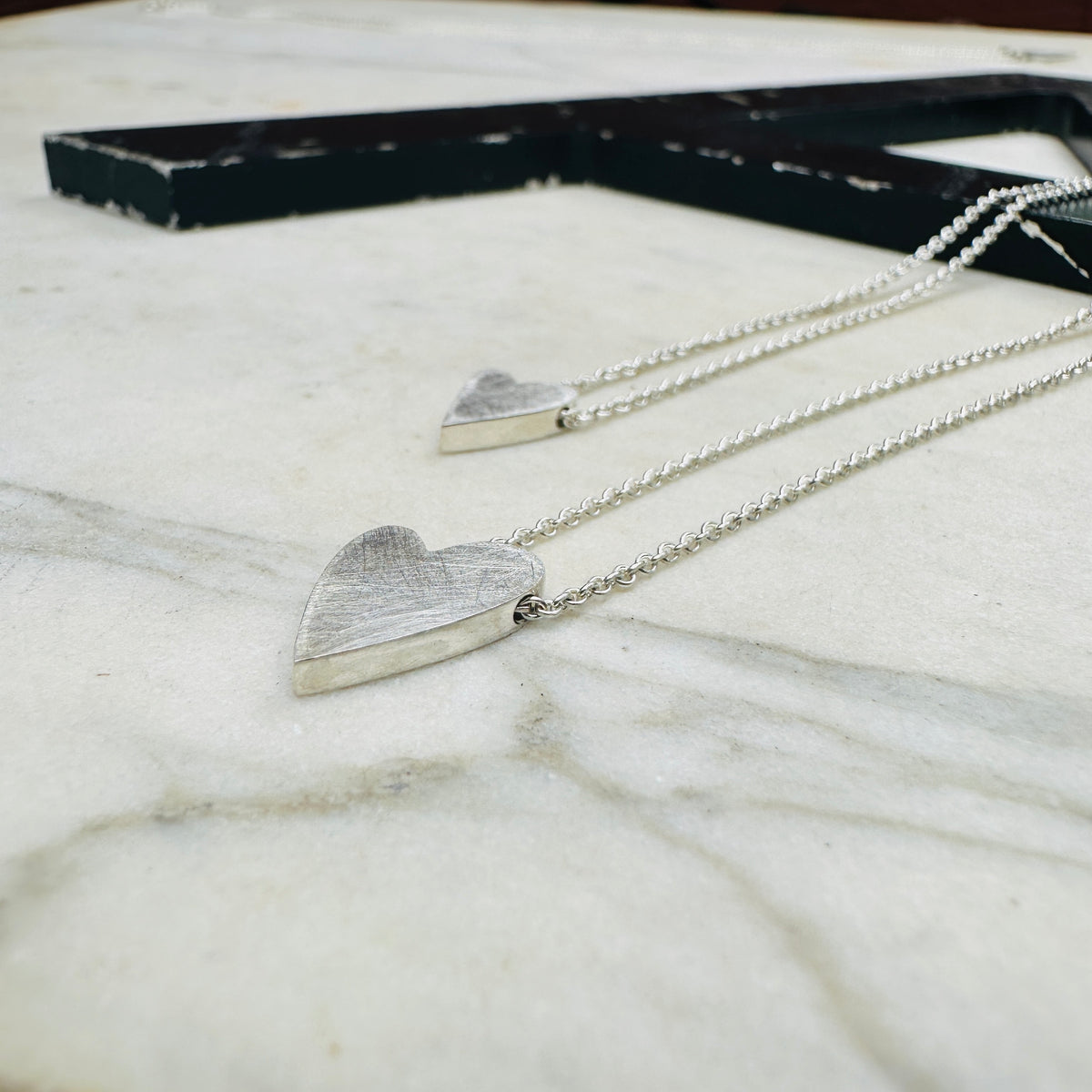 two sterling silver heart pendants in sterling silver on a marble surface 