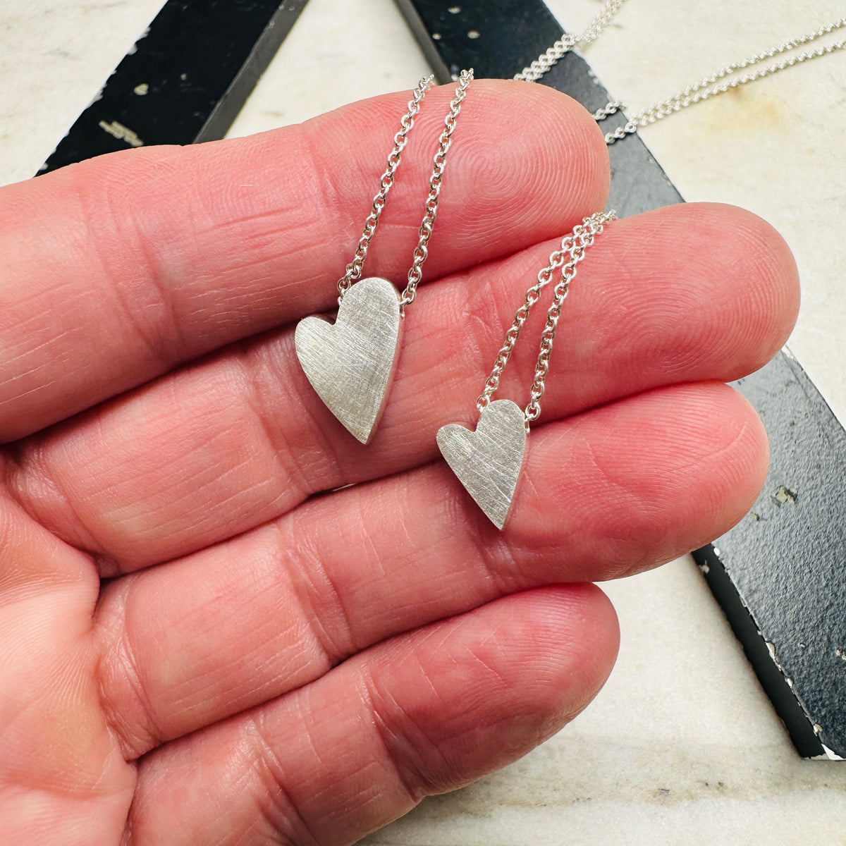 two sterling silver heart pendants in sterling silver on a marble surface in hand for scale 