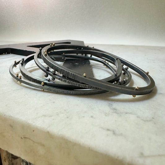 A set of oxidized sterling silver bangles with gold and silver rivets, arranged on a white marble surface.