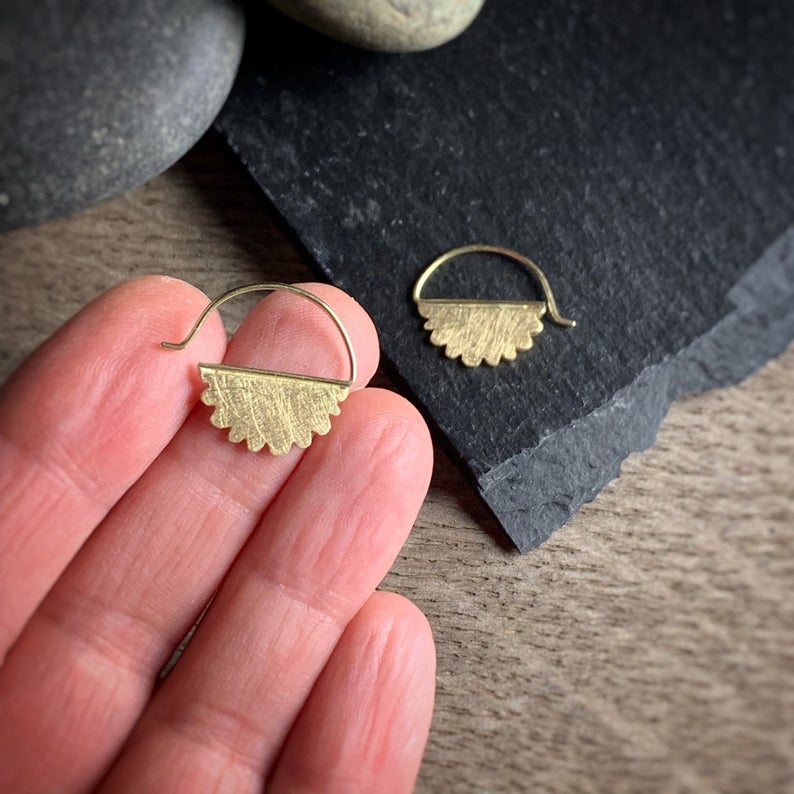 18k yellow gold scalloped edge cloud earrings on a hand for scale.