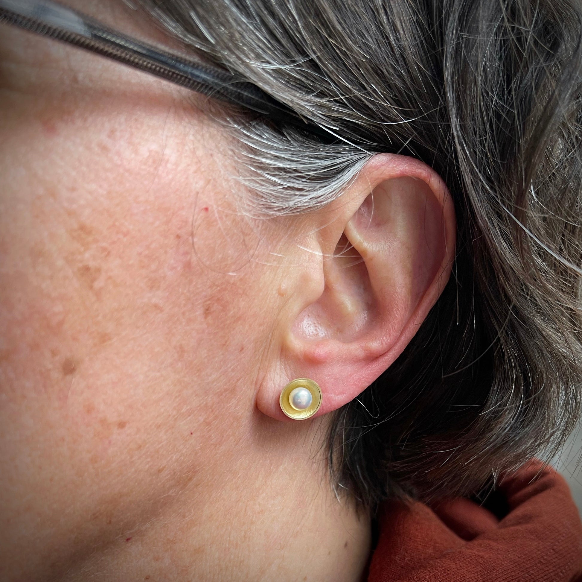 white pearls sit in yellow gold cups.  shown in the ear for scale