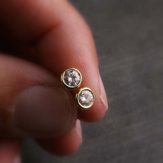 a pair of yellow gold Moissanite stud earrings held in a hand for scale