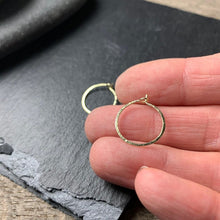 Load image into Gallery viewer, Small gold hoop earrings with a circle clasp shown on a hand for scale.
