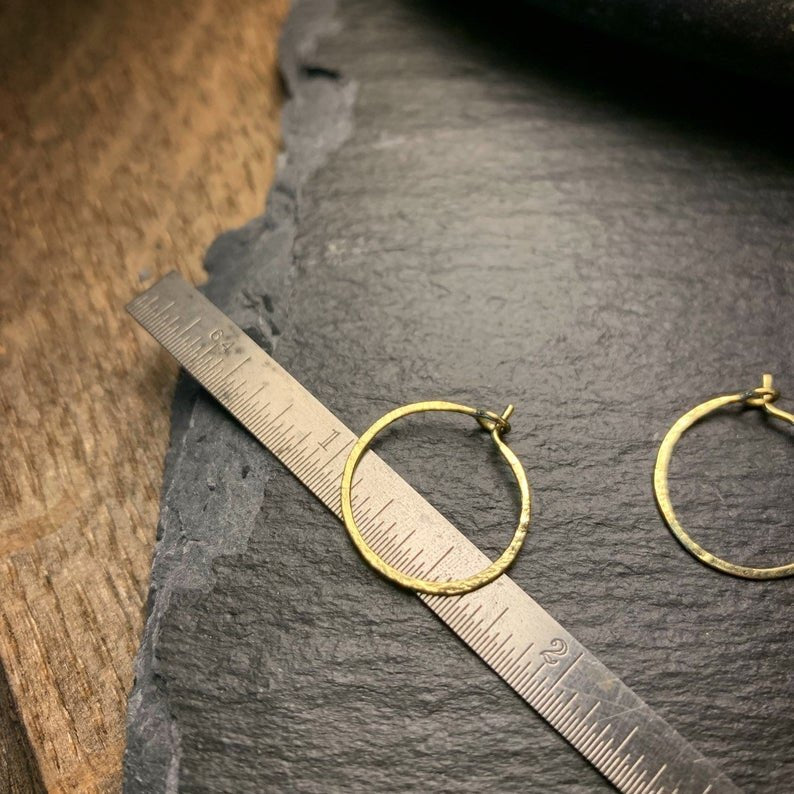 two small gold hoop earrings with a hammer texture shown on a ruler for size.