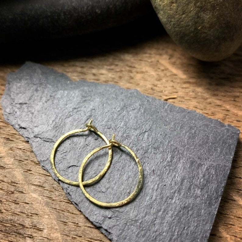 two small hammered textured hoop earrings in yellow gold.