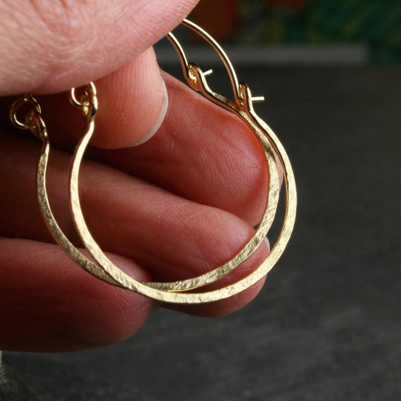 two hammered hoop earrings in yellow gold.  shown on a hand for scale