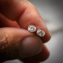 Load image into Gallery viewer, 14k rose gold bezel set Moissanite stud earrings shown being held in a hand for scale
