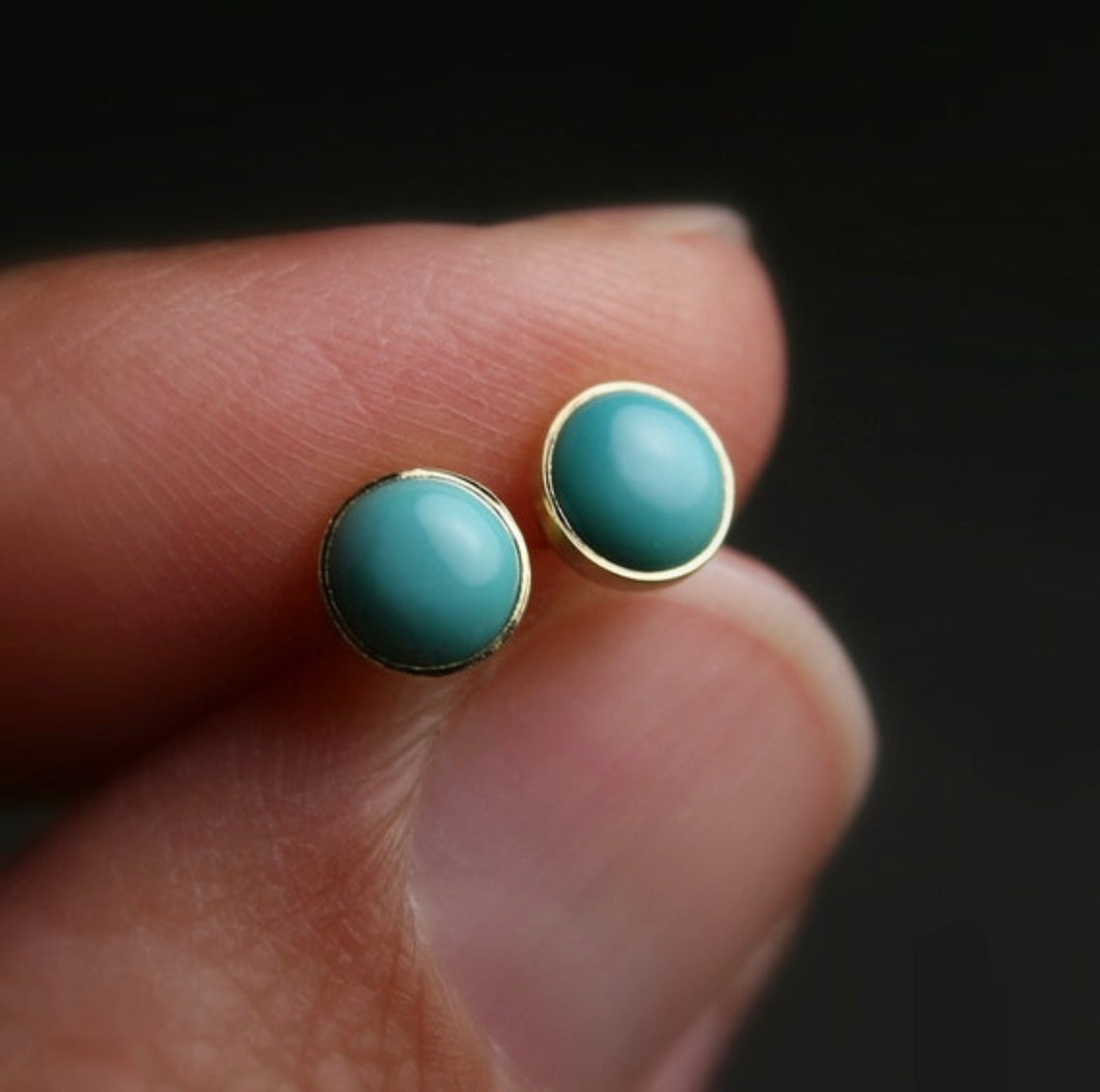 5mm nevada turquoise stud earrings set in 18k yellow gold shown being held in a hand for scale