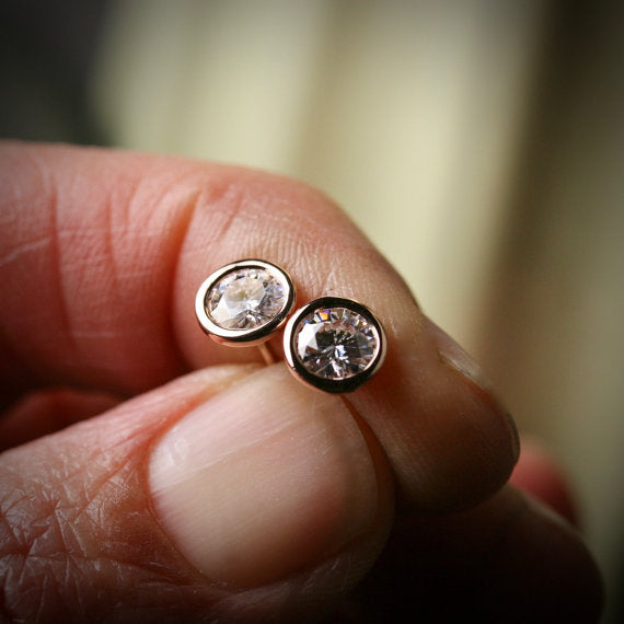 large 5mm Moissanite stud earrings in 14k rose gold bezels shown being held in a hand for scale