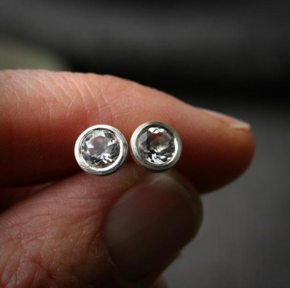 5mm white topaz bezel set earrings in sterling silver.  Shown being held in a hand for scale. 