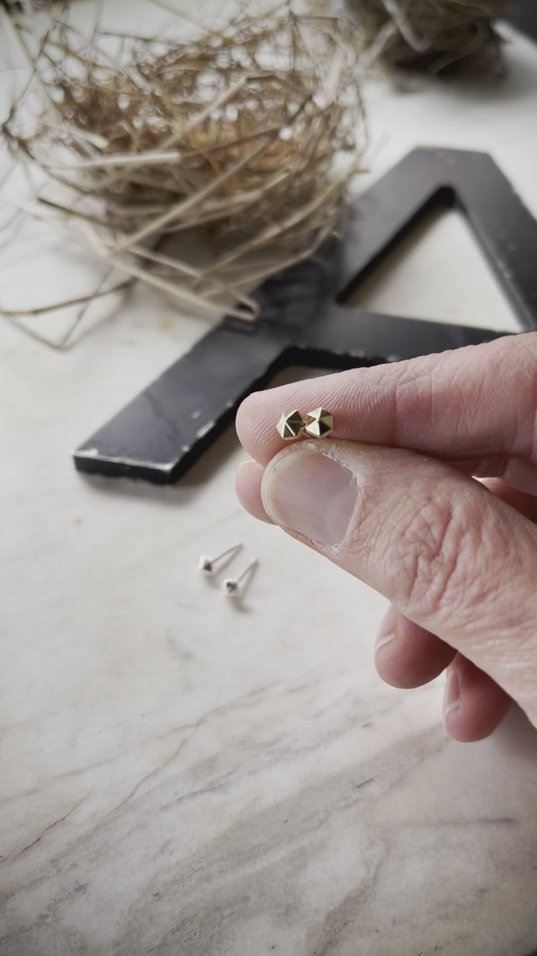 A video showing 14k yellow gold tiny hexagonal stud earrings being held in a hand.  The video shows the facets