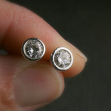 Load image into Gallery viewer, 5mm bezel set Moissanite stud earrings in sterling silver.  shown being held in a hand for scale

