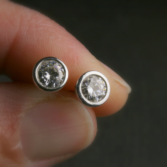 5mm bezel set Moissanite stud earrings in sterling silver.  shown being held in a hand for scale
