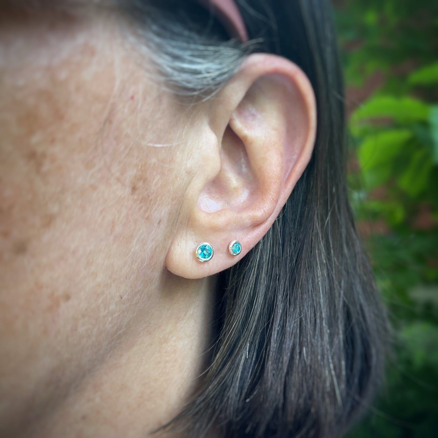 two sizes of bright blue topaz set in sterling silver bezels.  both sizes shown on a model for scale