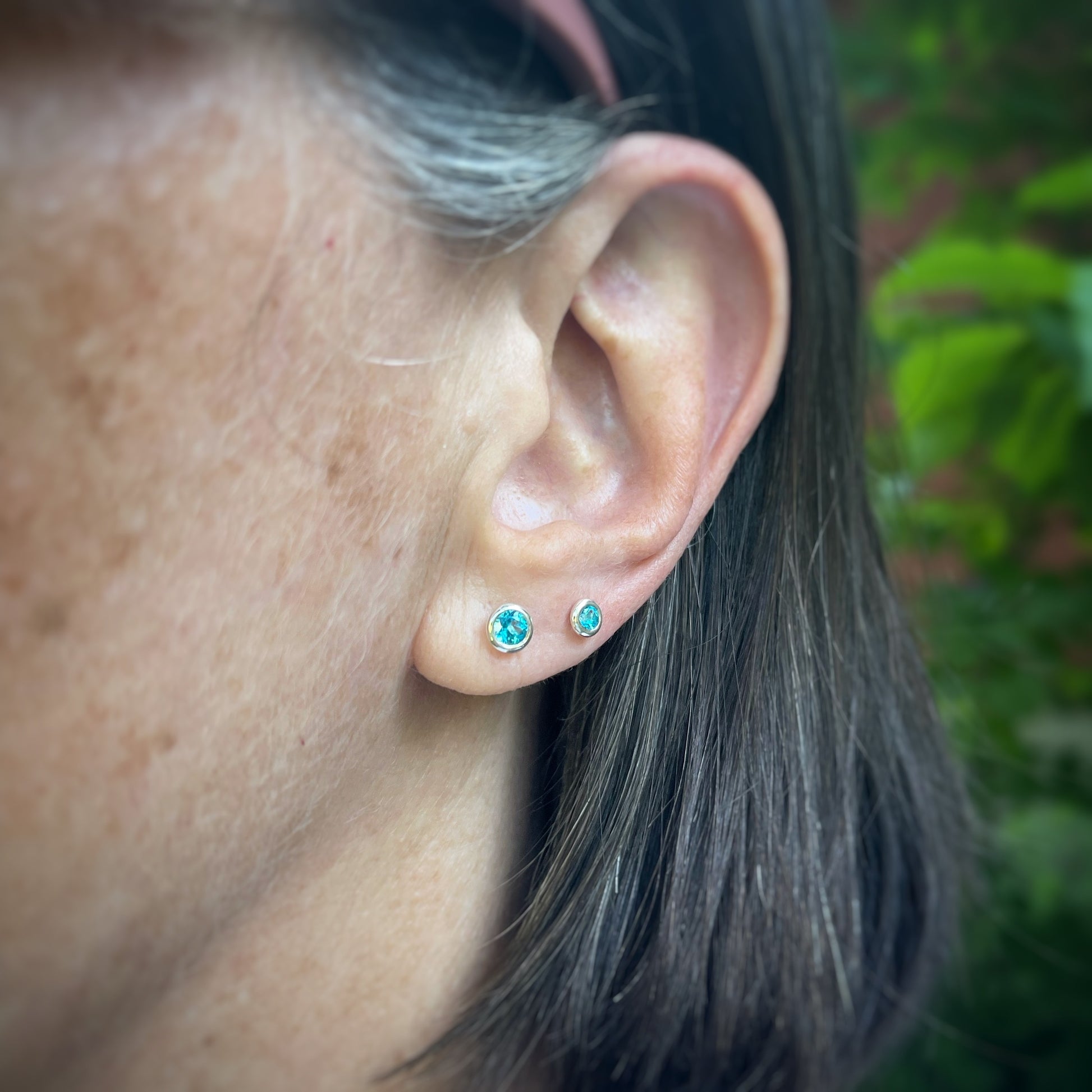 two sizes of bright blue topaz set in sterling silver bezels.  both sizes shown on a model for scale