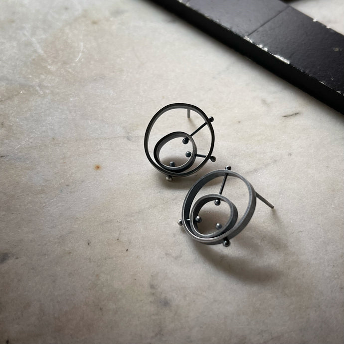 A pair of darkened silver earrings with concentric circles held in place by rivets