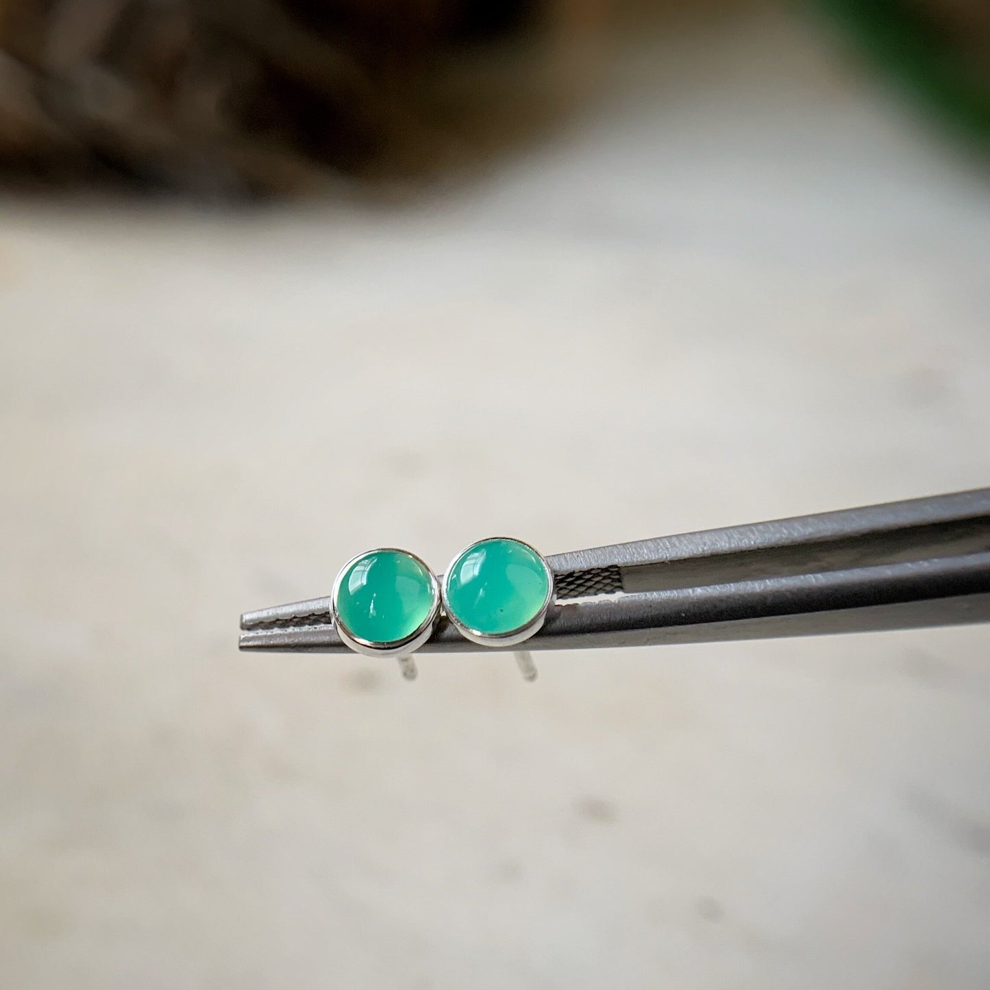 chrysoprase stud earrings shown in a tweezers for scale