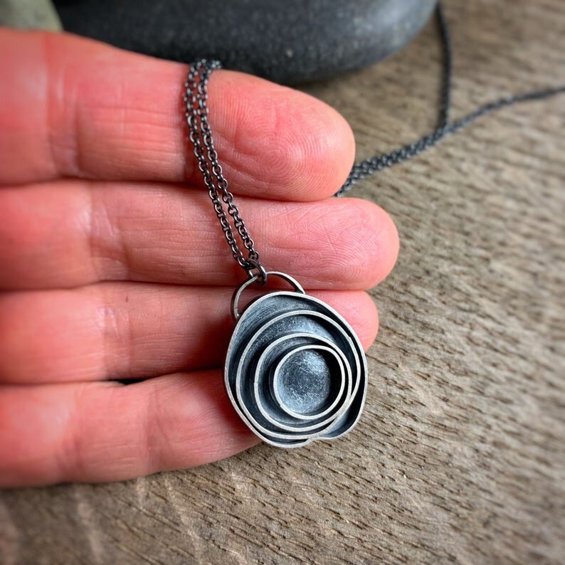 oxidized sterling silver pendant with concentric circles shown with a hand for scale