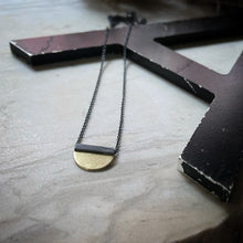 Load image into Gallery viewer, a half circle of yellow gold soldered to a oxidized silver square bail.  An oxidized chain runs through the bail. 
