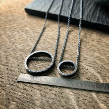 Load image into Gallery viewer, two pendants, one large and one small, in sterling silver.  They are circles with a hammered texture and the chain runs through the circle.  One is darkened silver and the other bright silver.  Shown on a ruler for scale.
