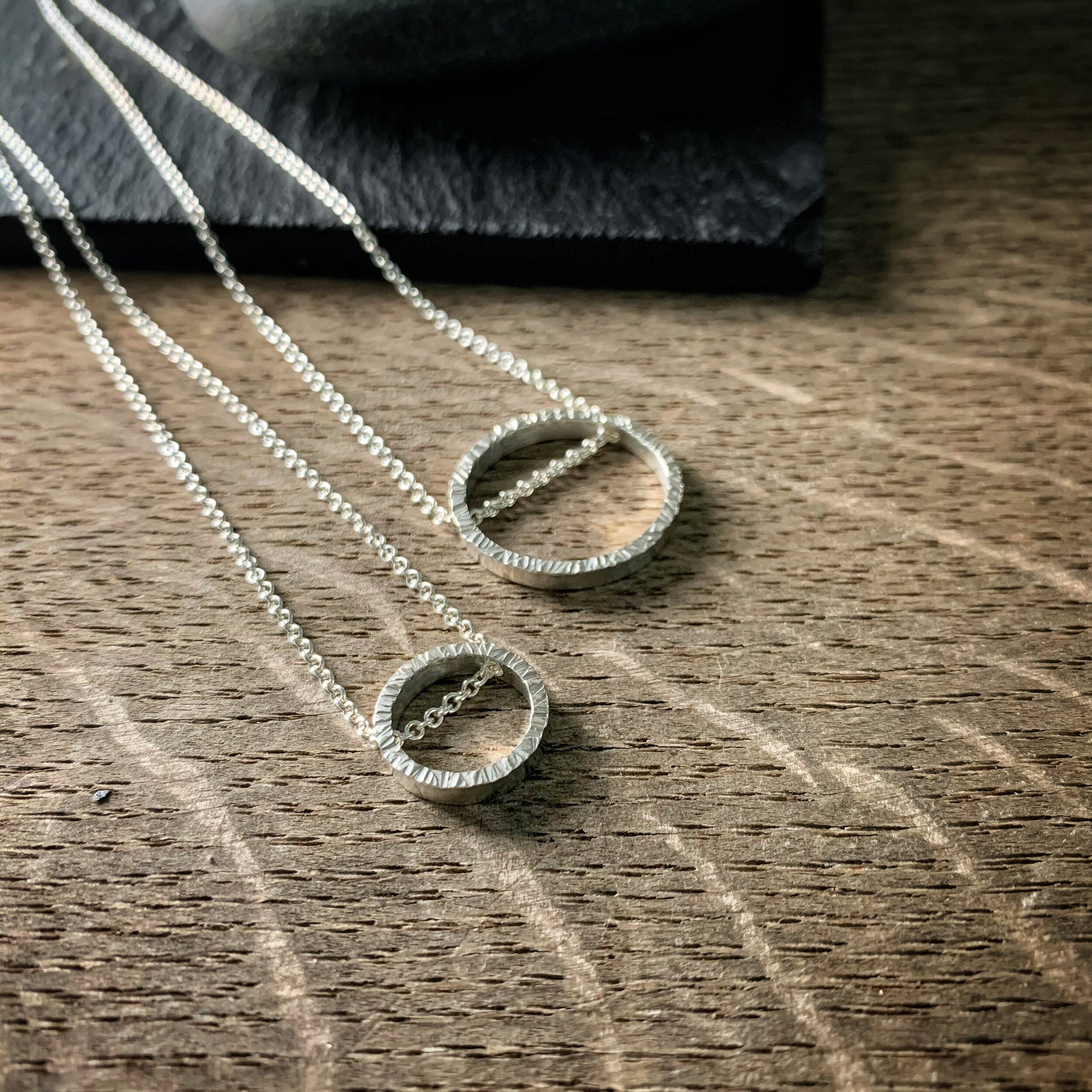 two pendants, one large and one small, in sterling silver.  They are circles with a hammered texture and the chain runs through the circle.  both are bright silver