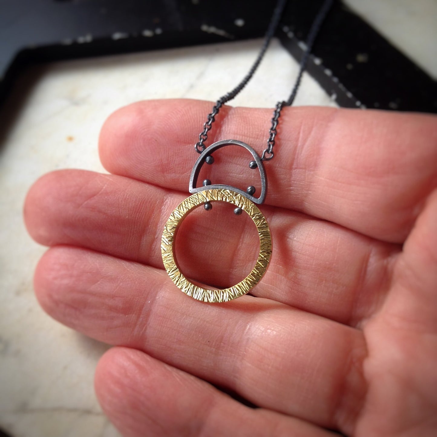 large textured gold circle with half circle sterling silver bail and silver chain pendant.  Shown in a hand for scale.