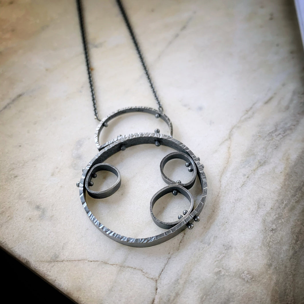 hammered organic circle with three more cells attached inside.  Oxidized sterling silver modern