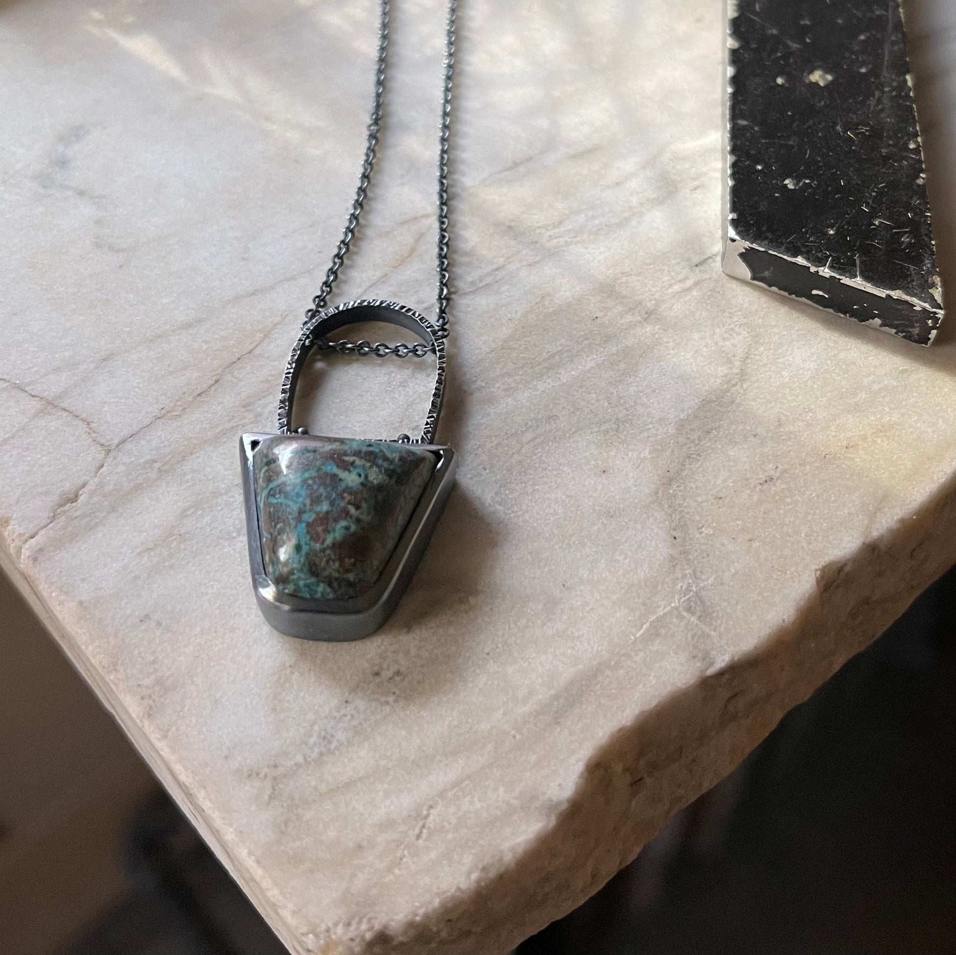 a blue green and brown stone in a oxidized bezel setting