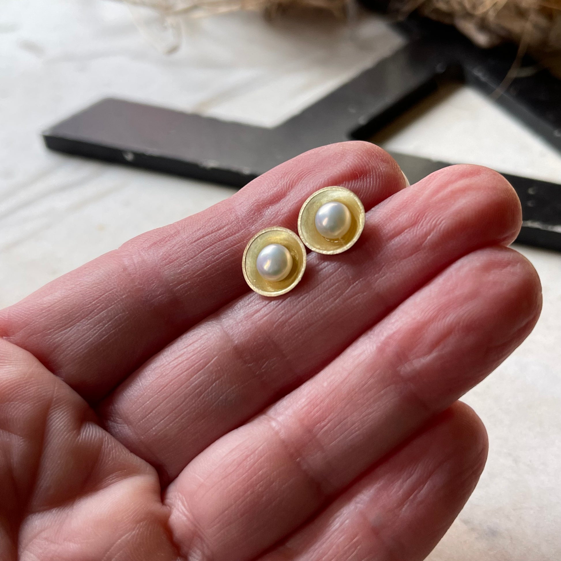 yellow gold and pearl earrings shown on a hand for scale