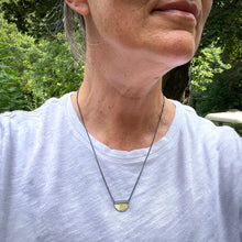 Load image into Gallery viewer, a half circle of yellow gold soldered to a oxidized silver square bail.  An oxidized chain runs through the bail.  Shown being worn for scale

