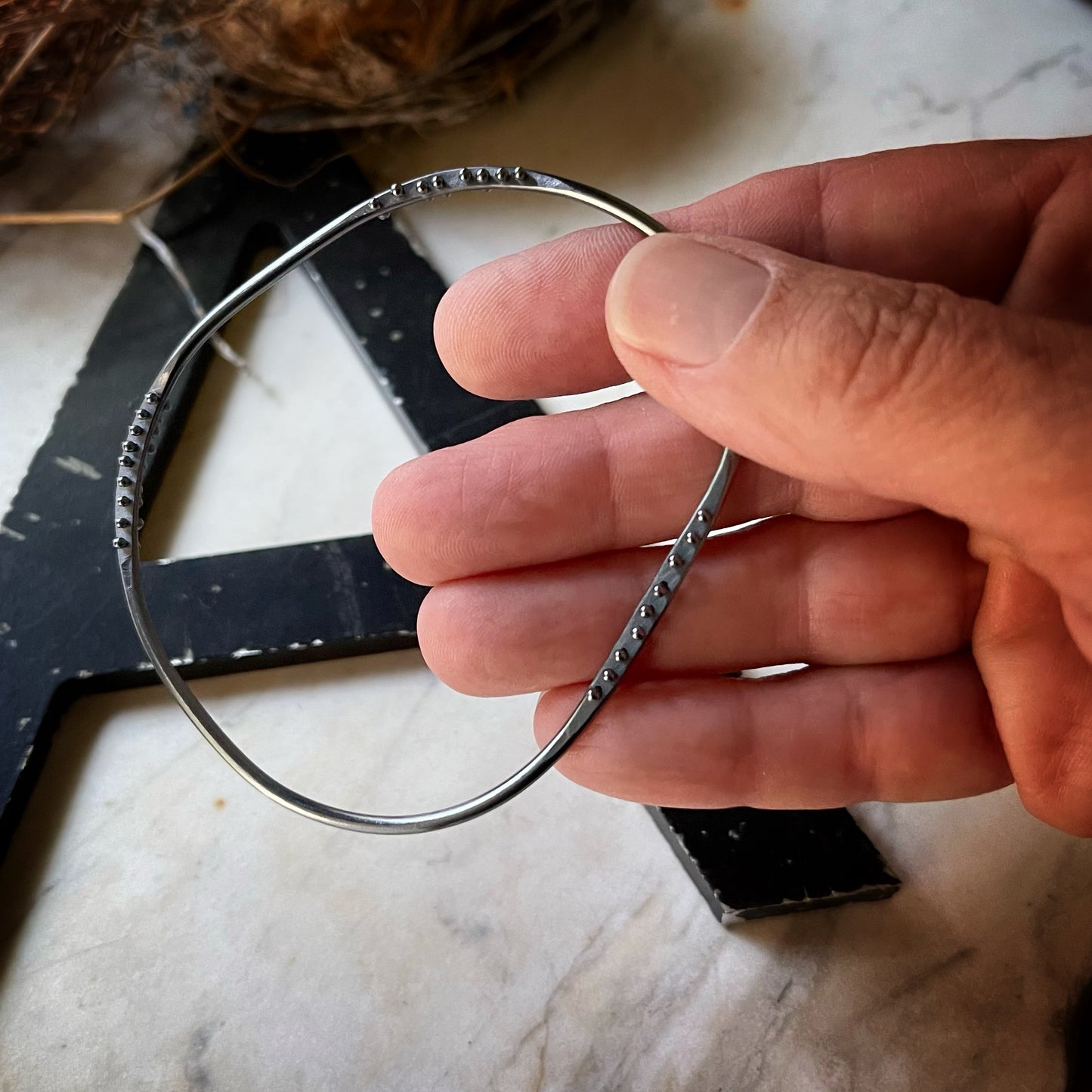 oxidized silver bangle bracelet with three stations of silver pins being held in a hand to show scale