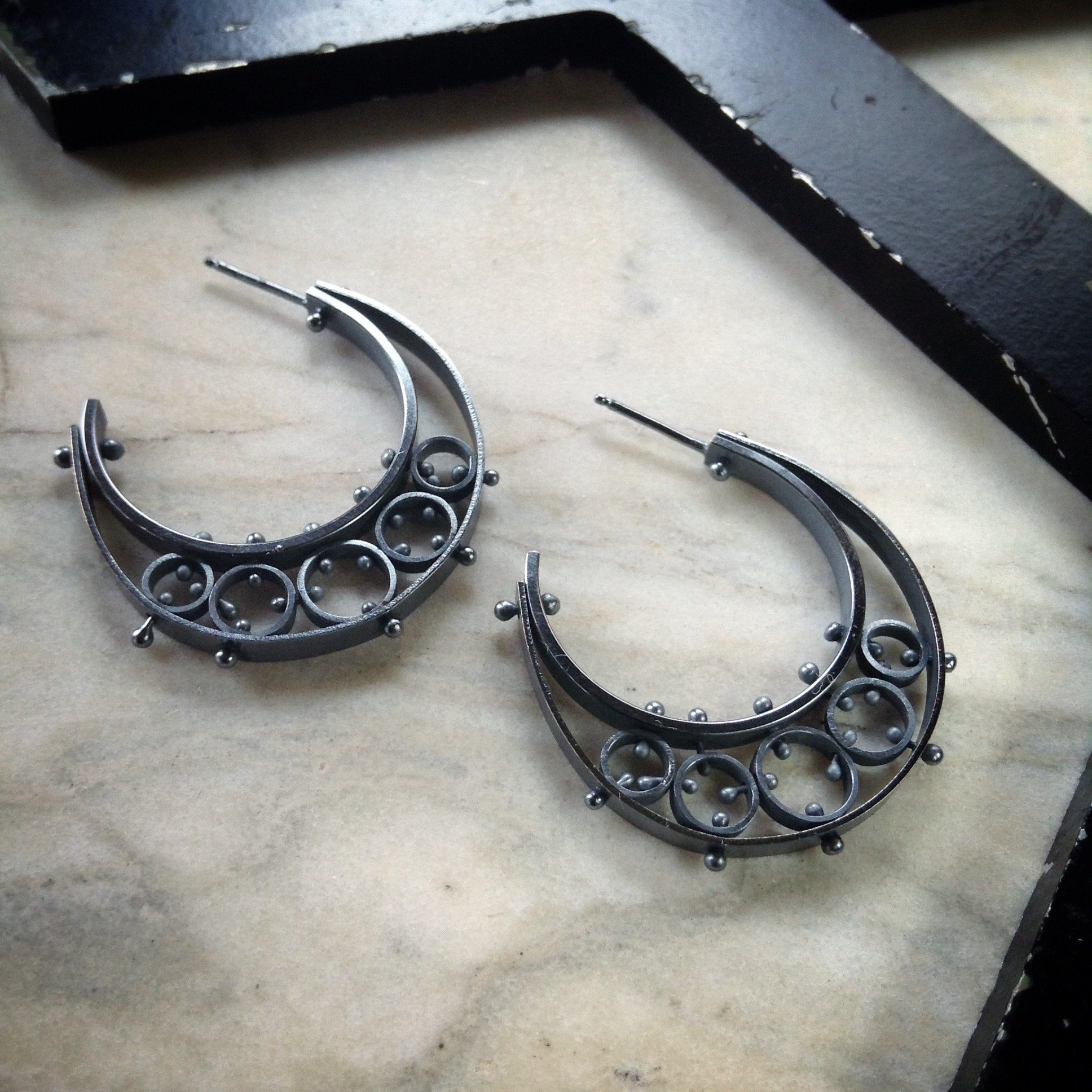 half moon hoop earrings in oxidized sterling sliver with several pinned circles