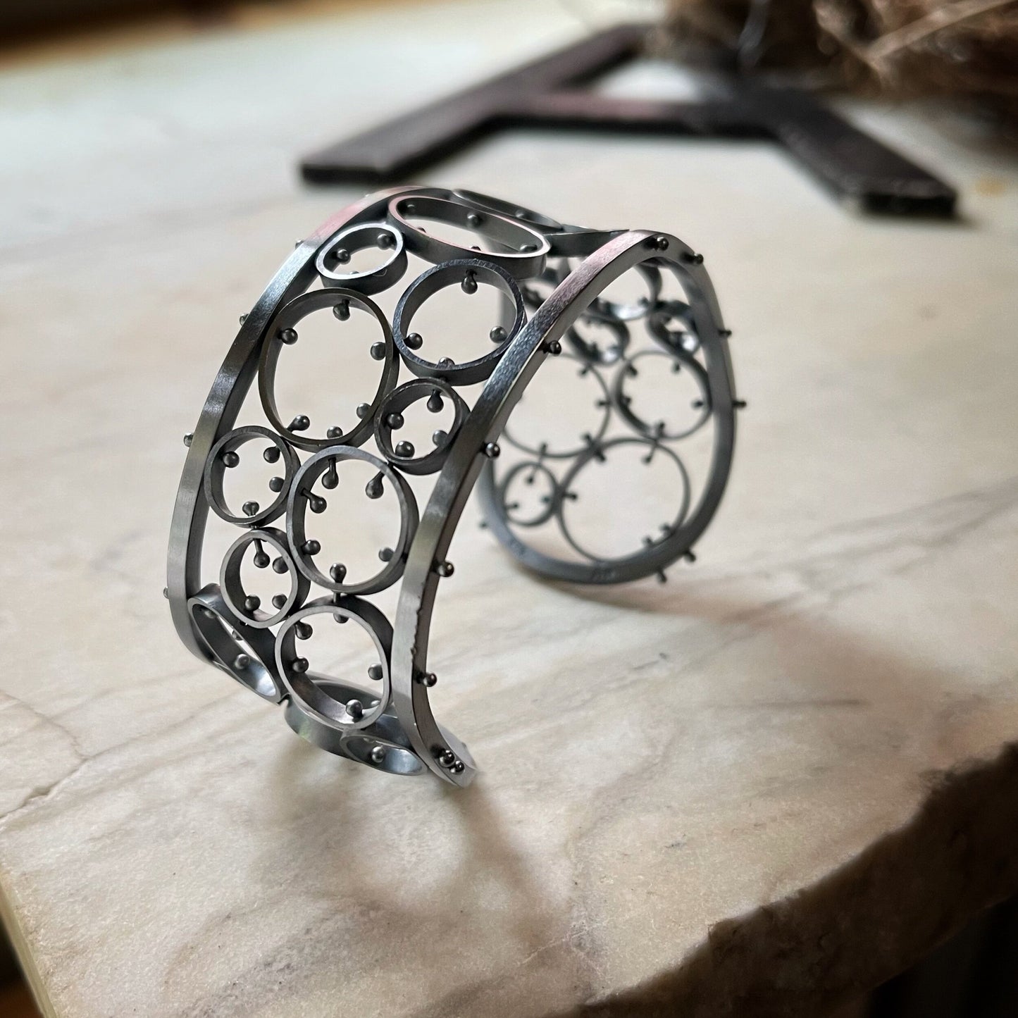 A sterling silver bracelet with a brushed finish and oxidized details, featuring a series of linked metal cells, displayed on a textured surface.