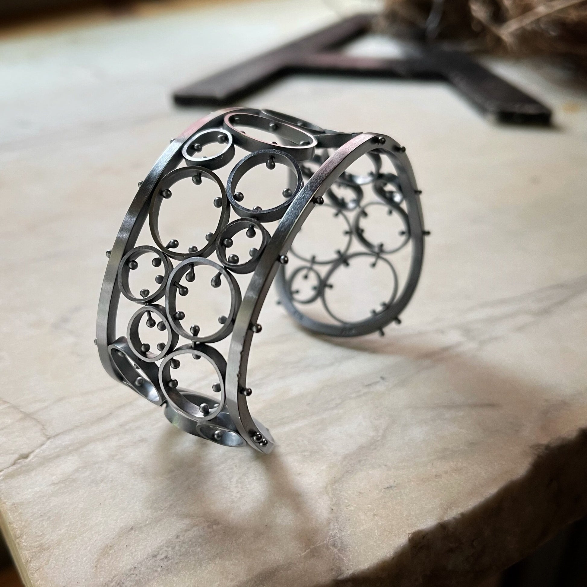 A sterling silver bracelet with a brushed finish and oxidized details, featuring a series of linked metal cells, displayed on a textured surface.