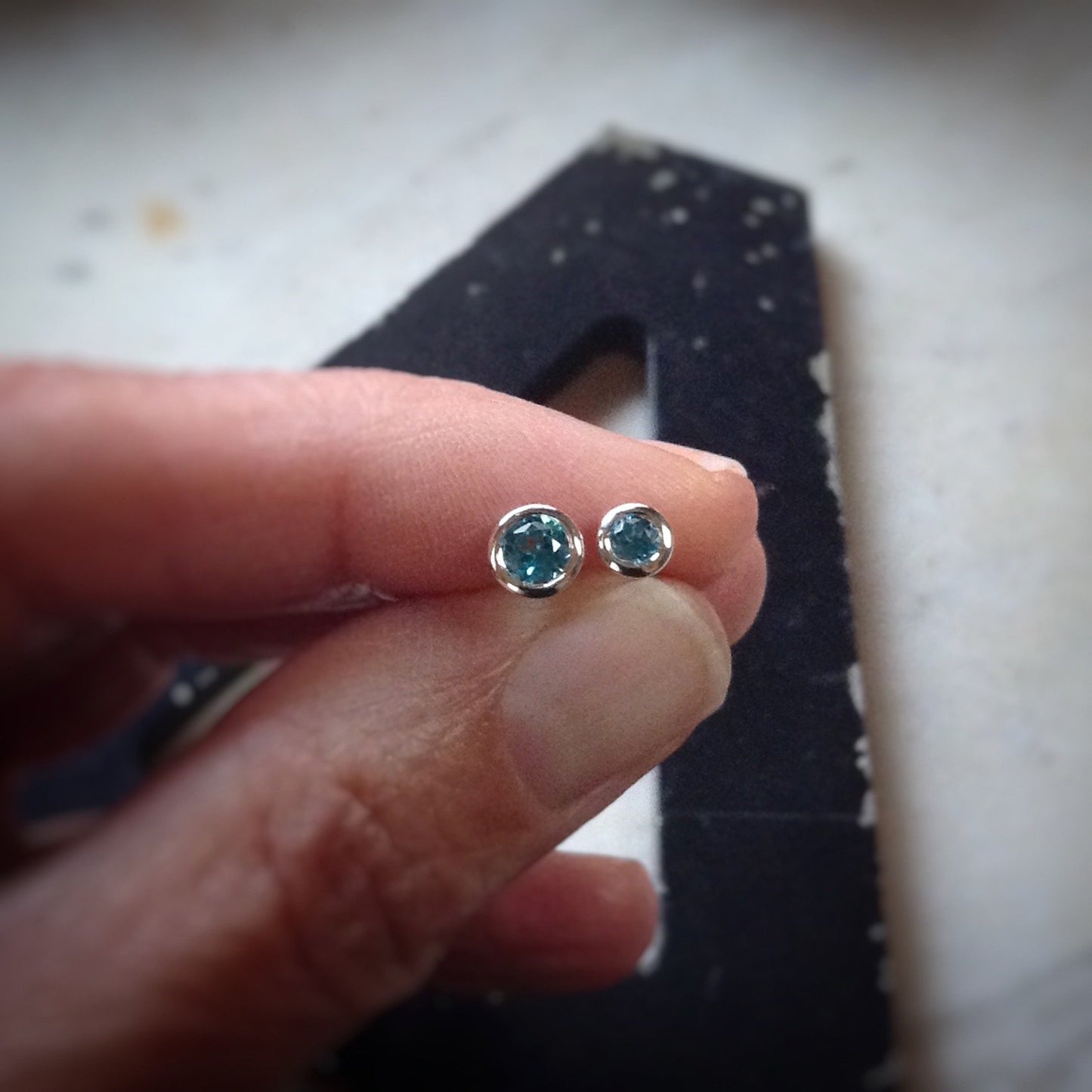 two sizes of bright blue topaz set in sterling silver bezels shown in a hand for scale